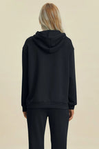 Person wearing a black hoodie and pants on a beige background