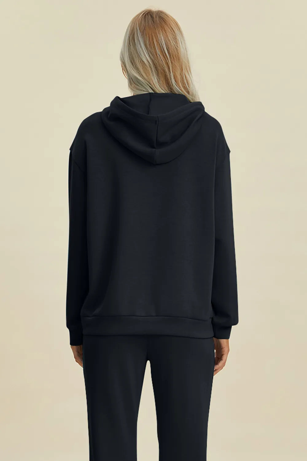 Person wearing a black hoodie and pants on a beige background