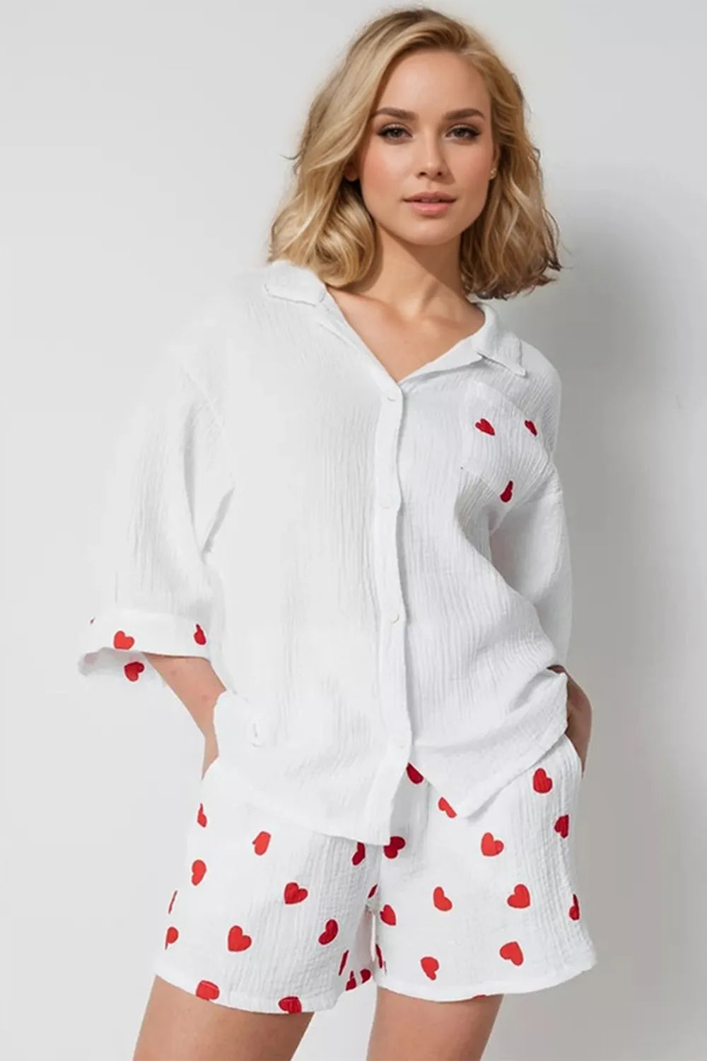 Woman wearing a white shirt and shorts with red heart patterns on a plain background
