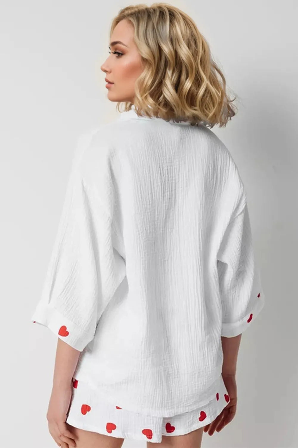 Woman wearing a white textured kimono-style top with red heart patterns on a plain background