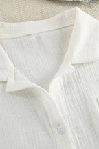 Close-up of a white shirt with a collar and button on a textured beige background