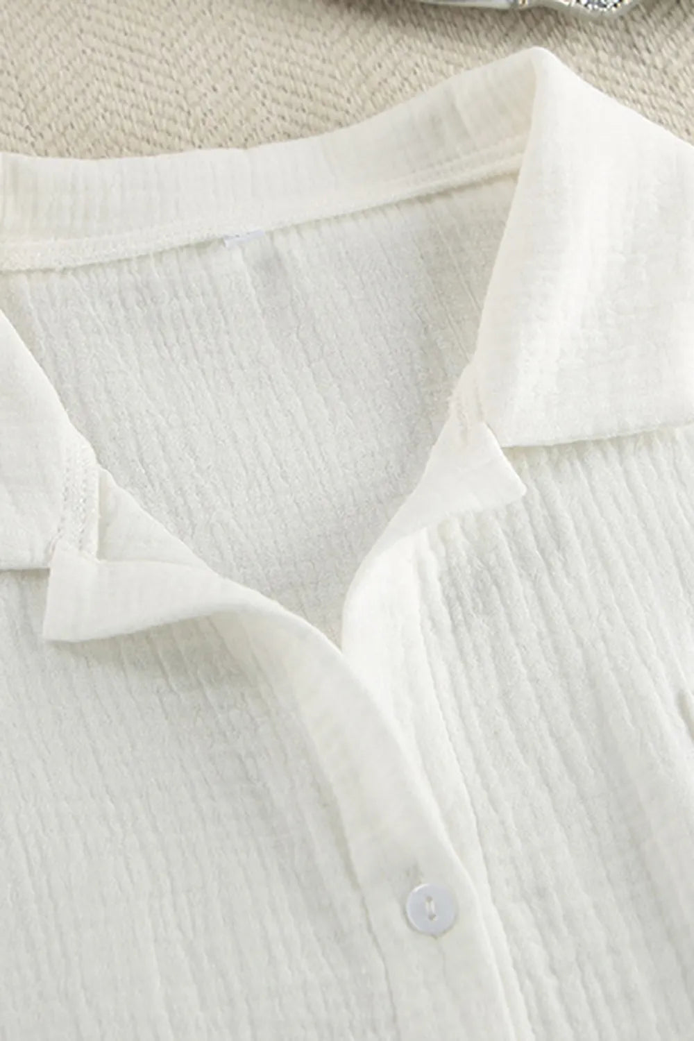 Close-up of a white shirt with a collar and button on a textured beige background
