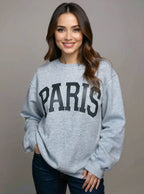 Woman wearing a gray sweatshirt with 'PARIS' printed on it against a plain background