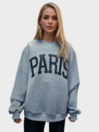 Woman wearing a gray sweatshirt with 'PARIS' printed on it against a plain background