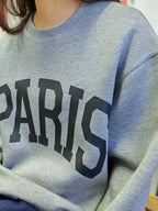 Gray sweatshirt with 'PARIS' printed on it, worn by a person.