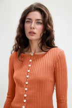 Woman wearing an orange ribbed sweater with buttons on a white background