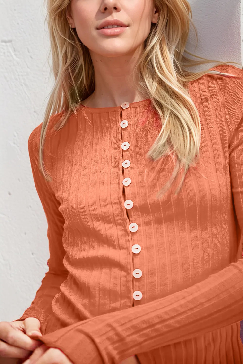 Woman wearing an orange textured top with buttons against a white wall