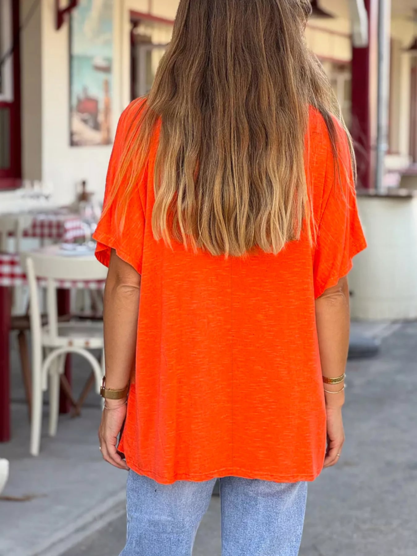 Person wearing an orange top with a blurred background of a street scene.