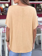 Person wearing a beige oversized t-shirt in an outdoor setting with tables and chairs.