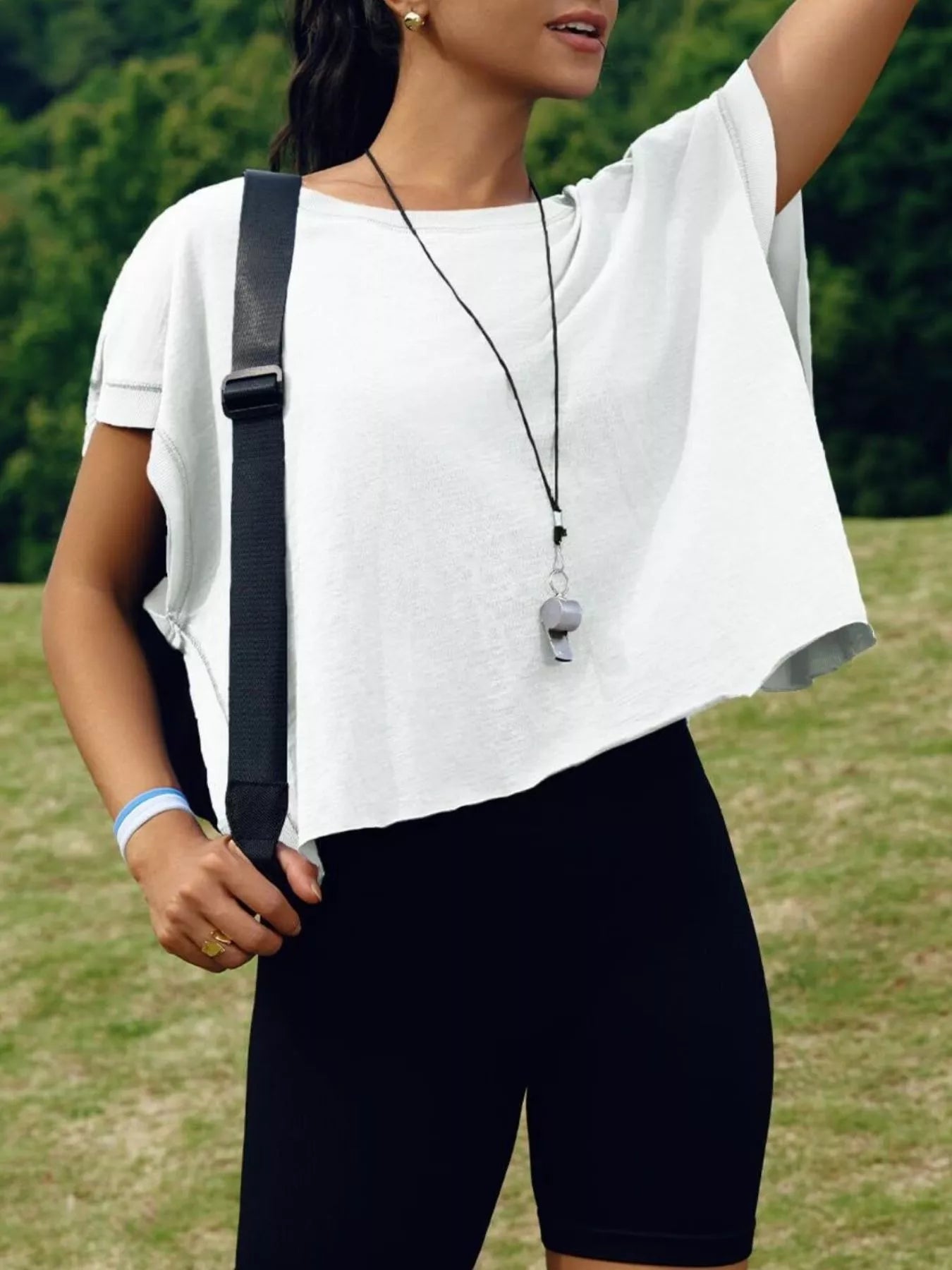 Woman wearing a white top and black shorts with a blurred green background