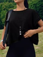 Person wearing a black outfit with a strap over one shoulder, standing outdoors.
