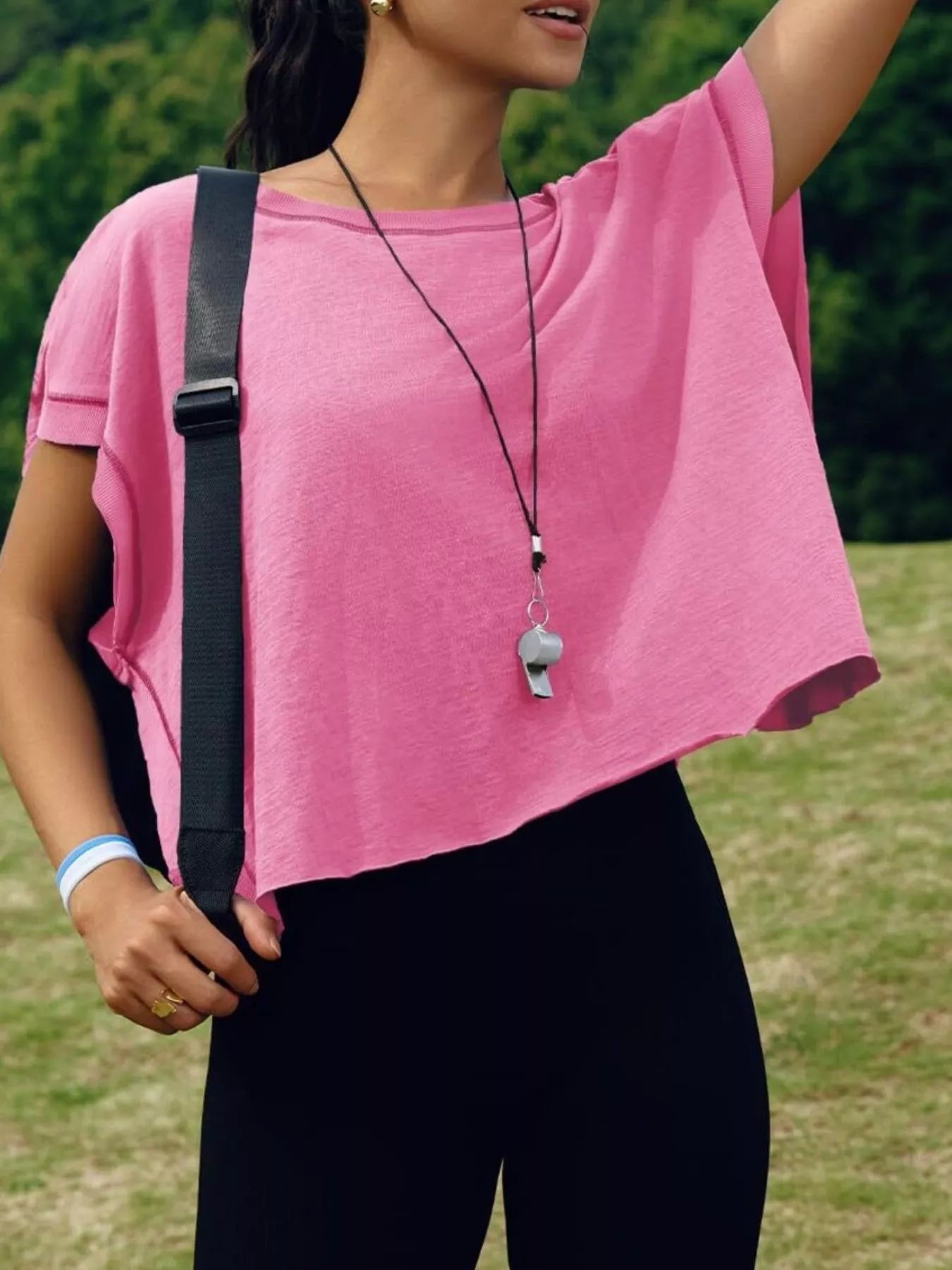 Person wearing a pink shirt and black pants with a whistle, standing outdoors.