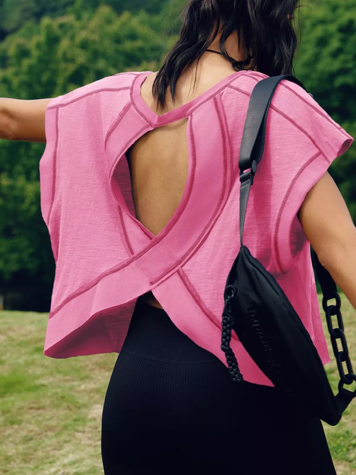 Person wearing a pink sleeveless top with a black bag over their shoulder outdoors.