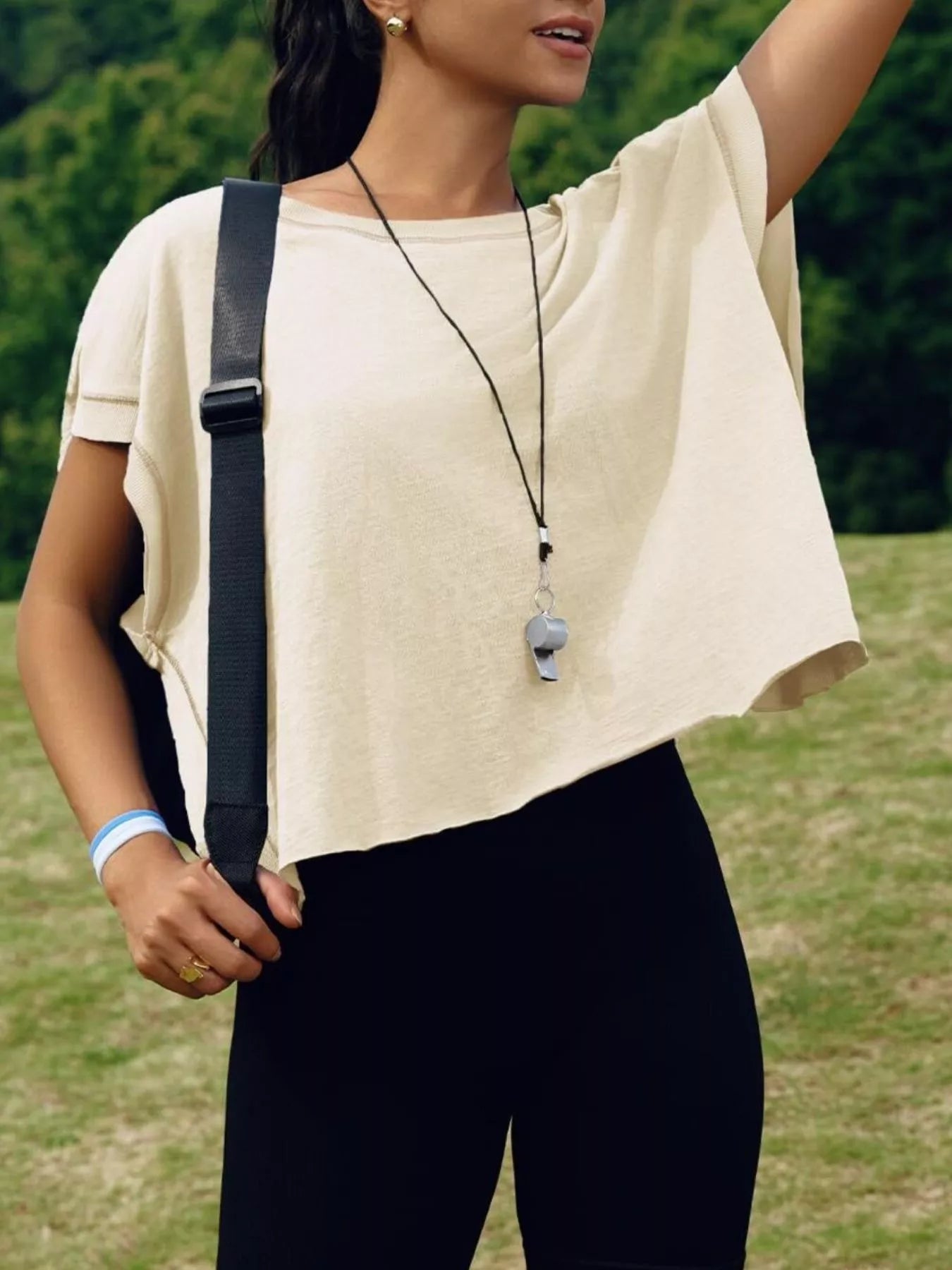 Person wearing a beige top and black pants with a necklace, standing outdoors.