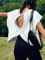 Person wearing a white sleeveless top and black leggings with a black bag over one shoulder, standing outdoors.