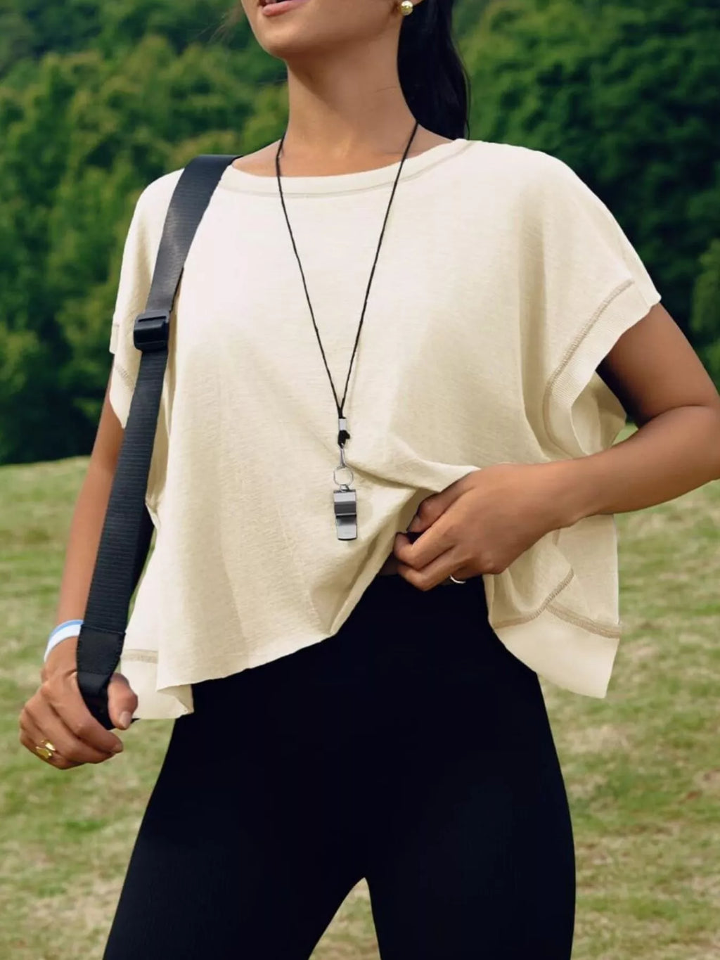 Person wearing a beige top and black pants with a blurred green background