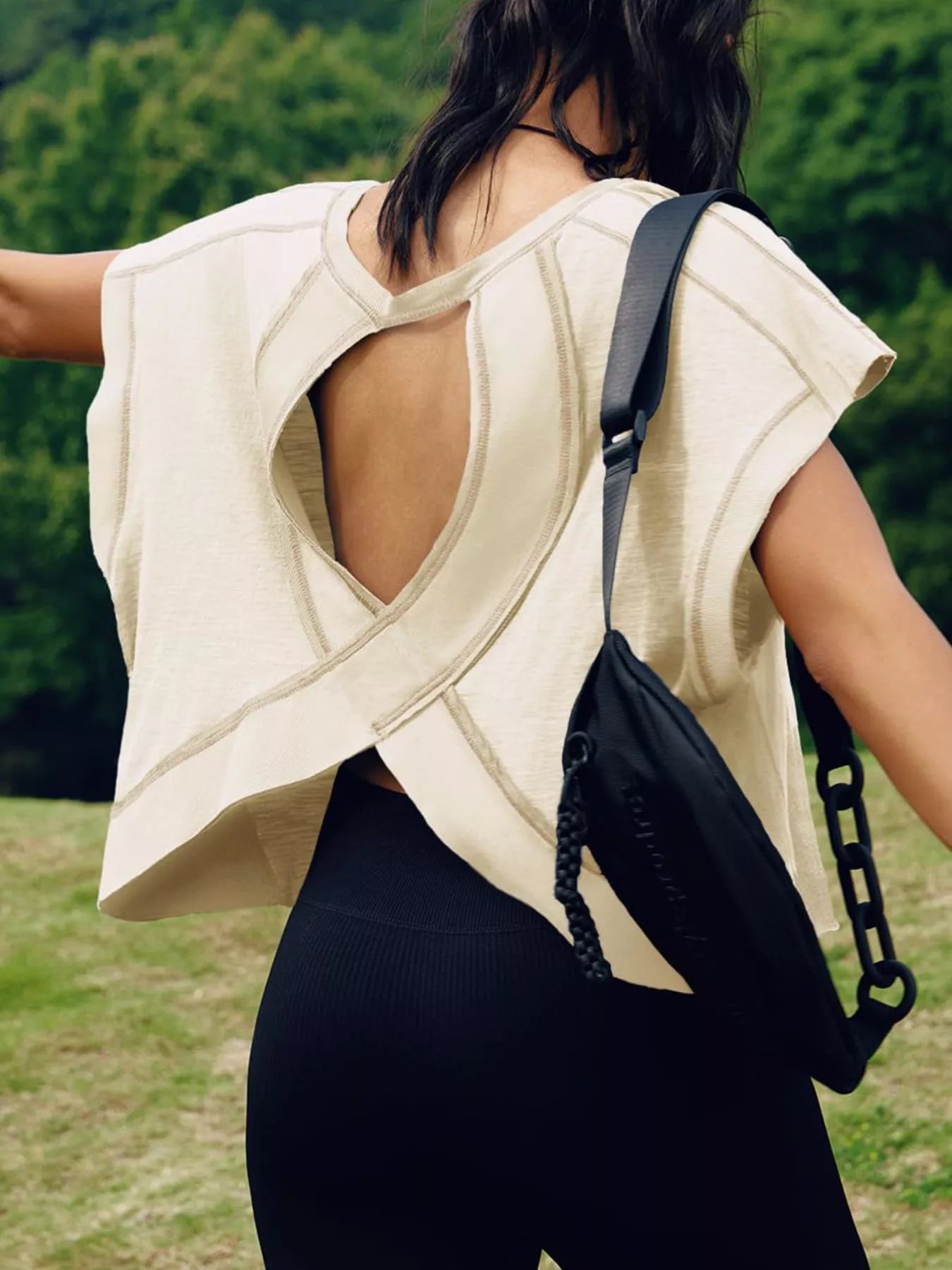Person wearing a beige open-back top and black pants with a black backpack outdoors.