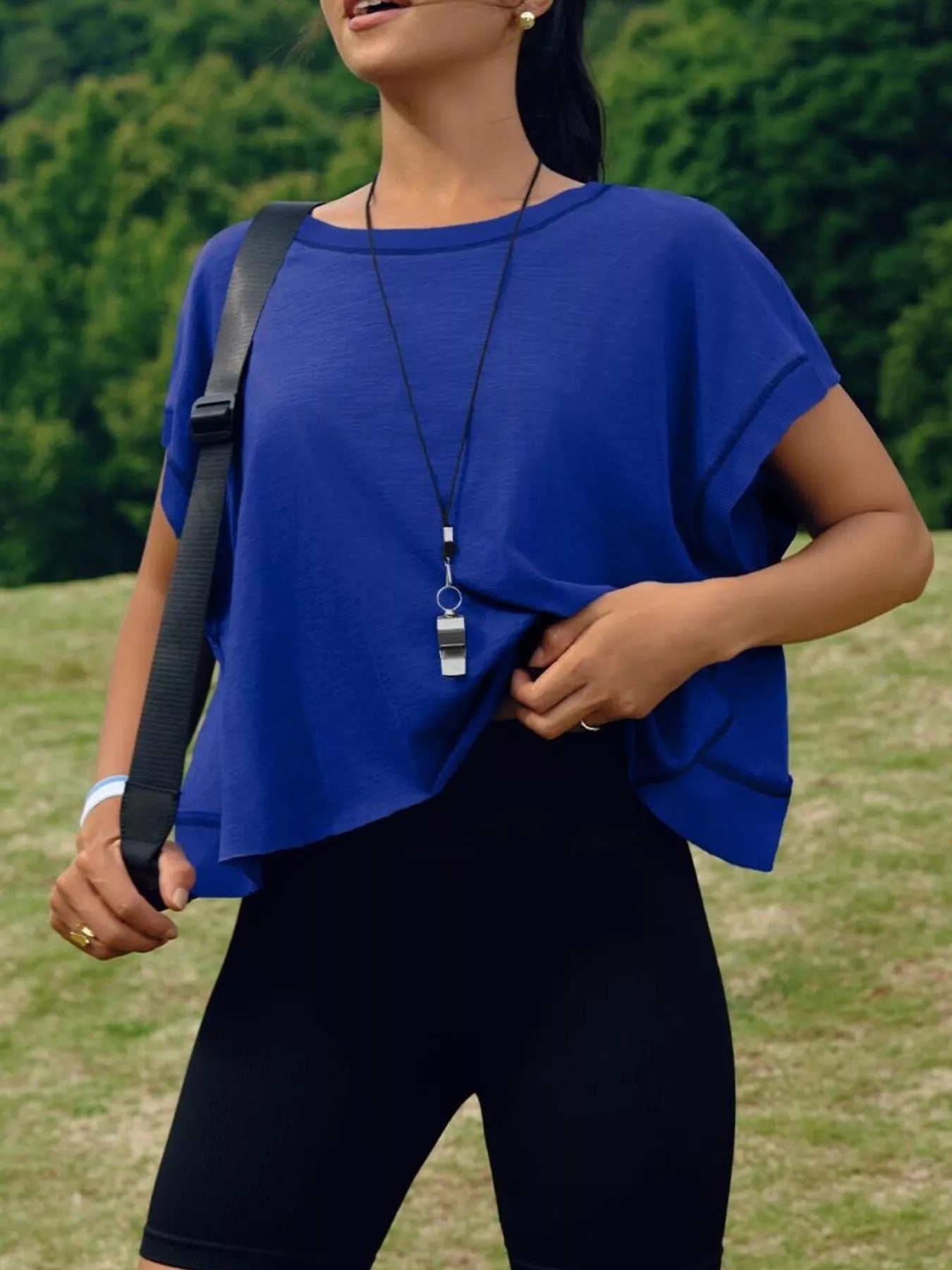 Person wearing a blue top and black pants outdoors with greenery in the background
