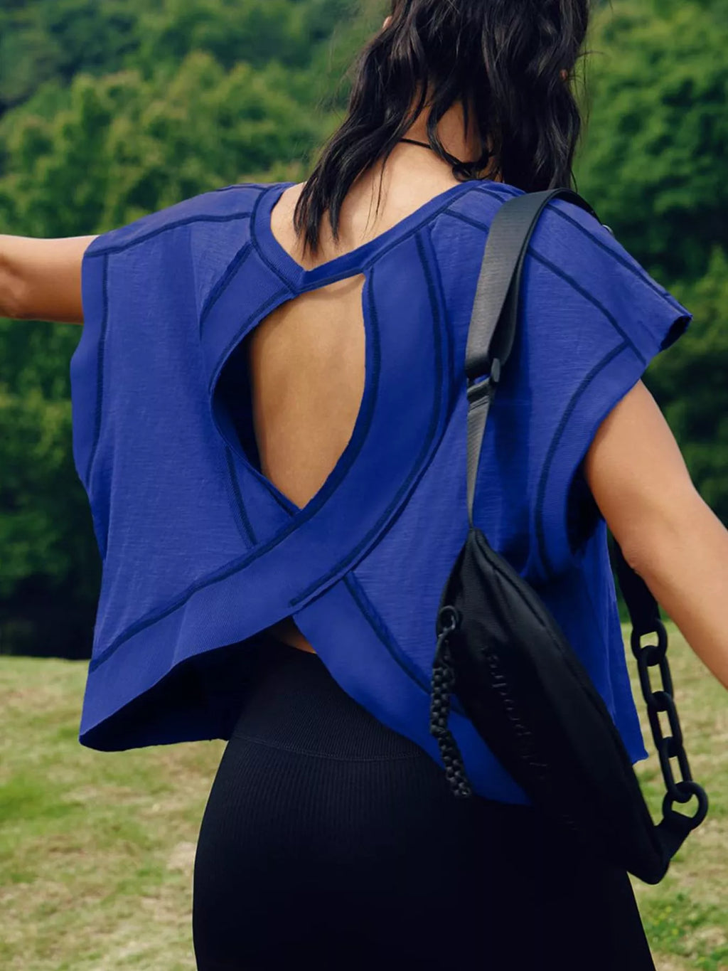 Person wearing a blue sleeveless top with a black bag over their shoulder outdoors.