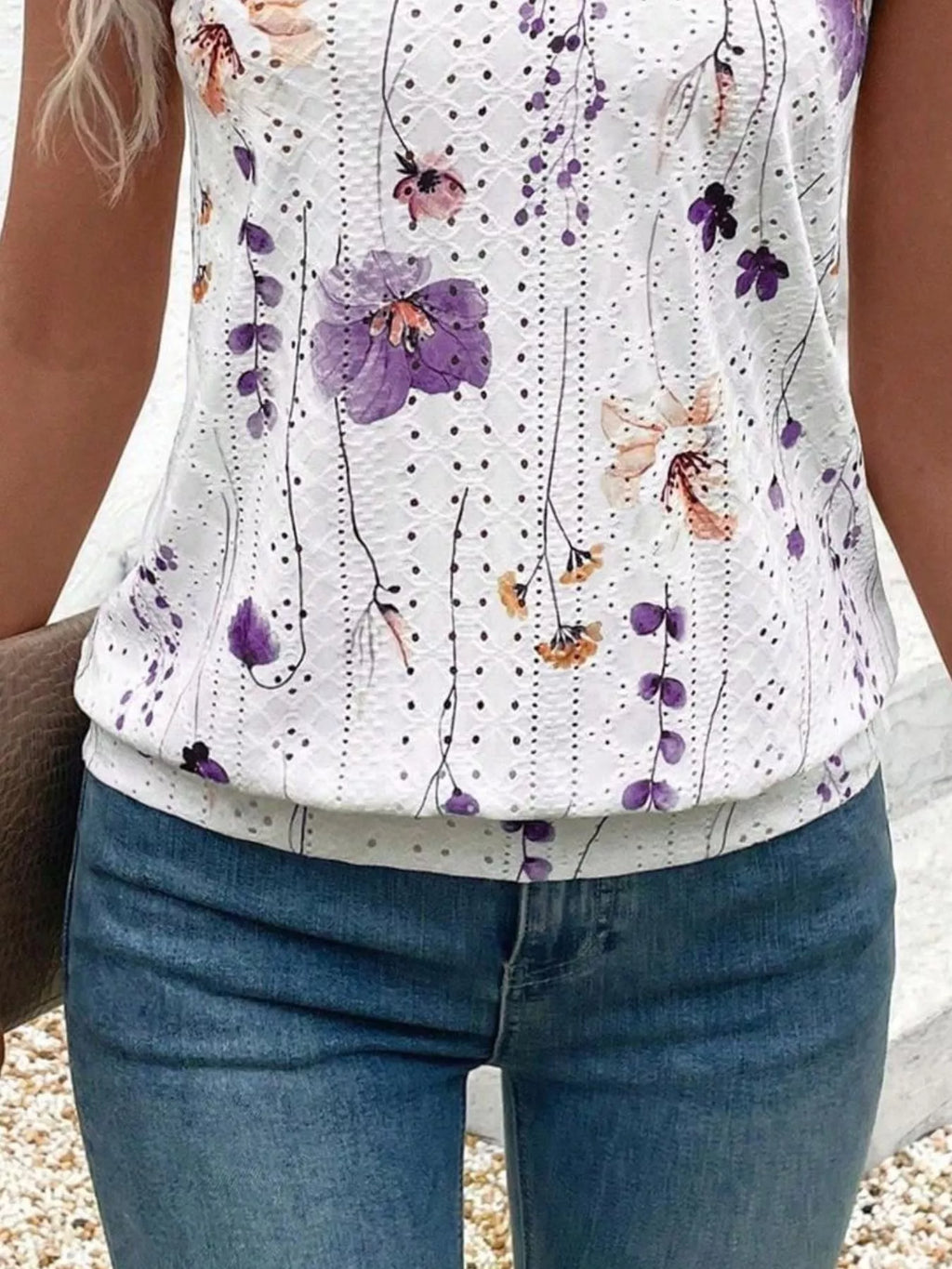 Person wearing a white sleeveless top with floral patterns and blue jeans.