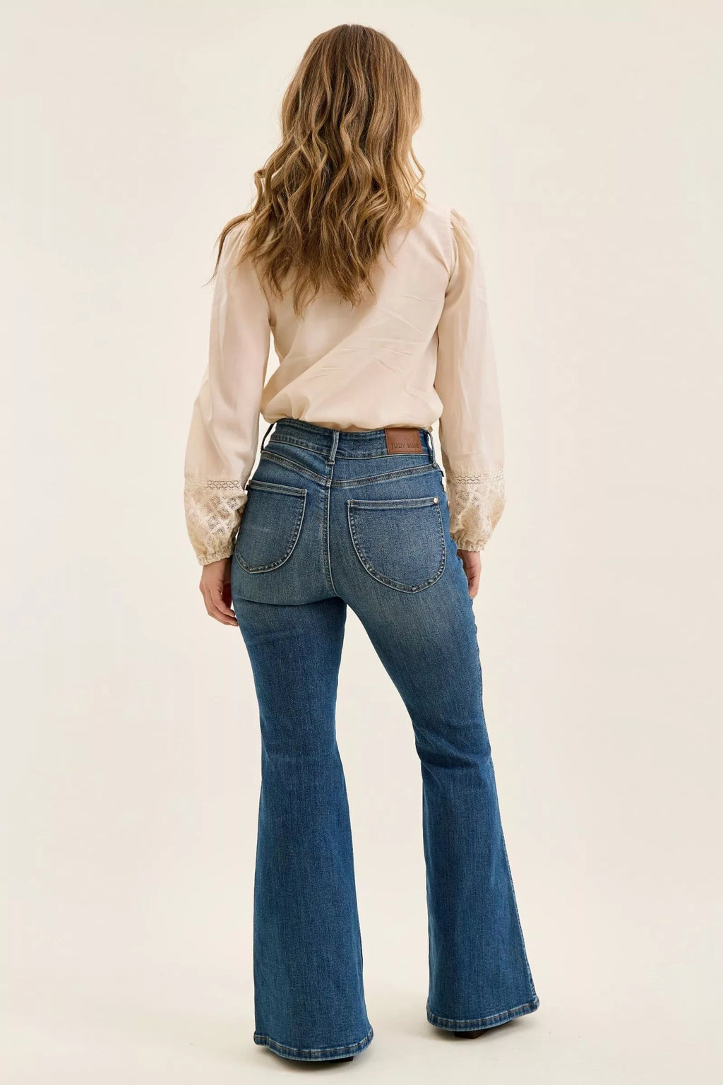 Person wearing blue flared jeans and a beige blouse on a plain background