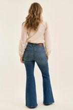 Person wearing blue flared jeans and a beige blouse on a plain background