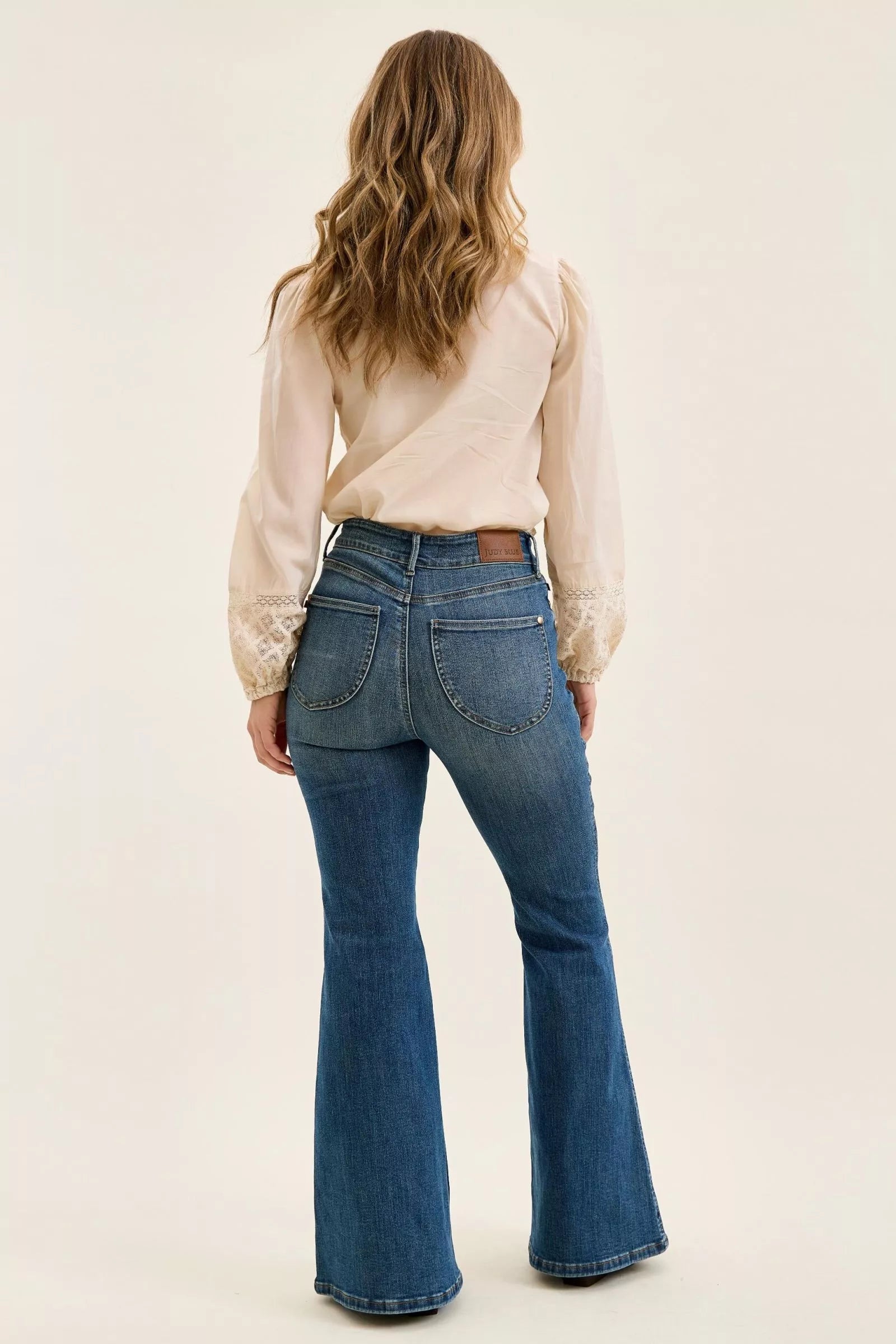 Person wearing blue flared jeans and a beige blouse on a plain background