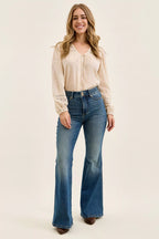 Woman wearing a beige blouse and blue jeans on a plain background