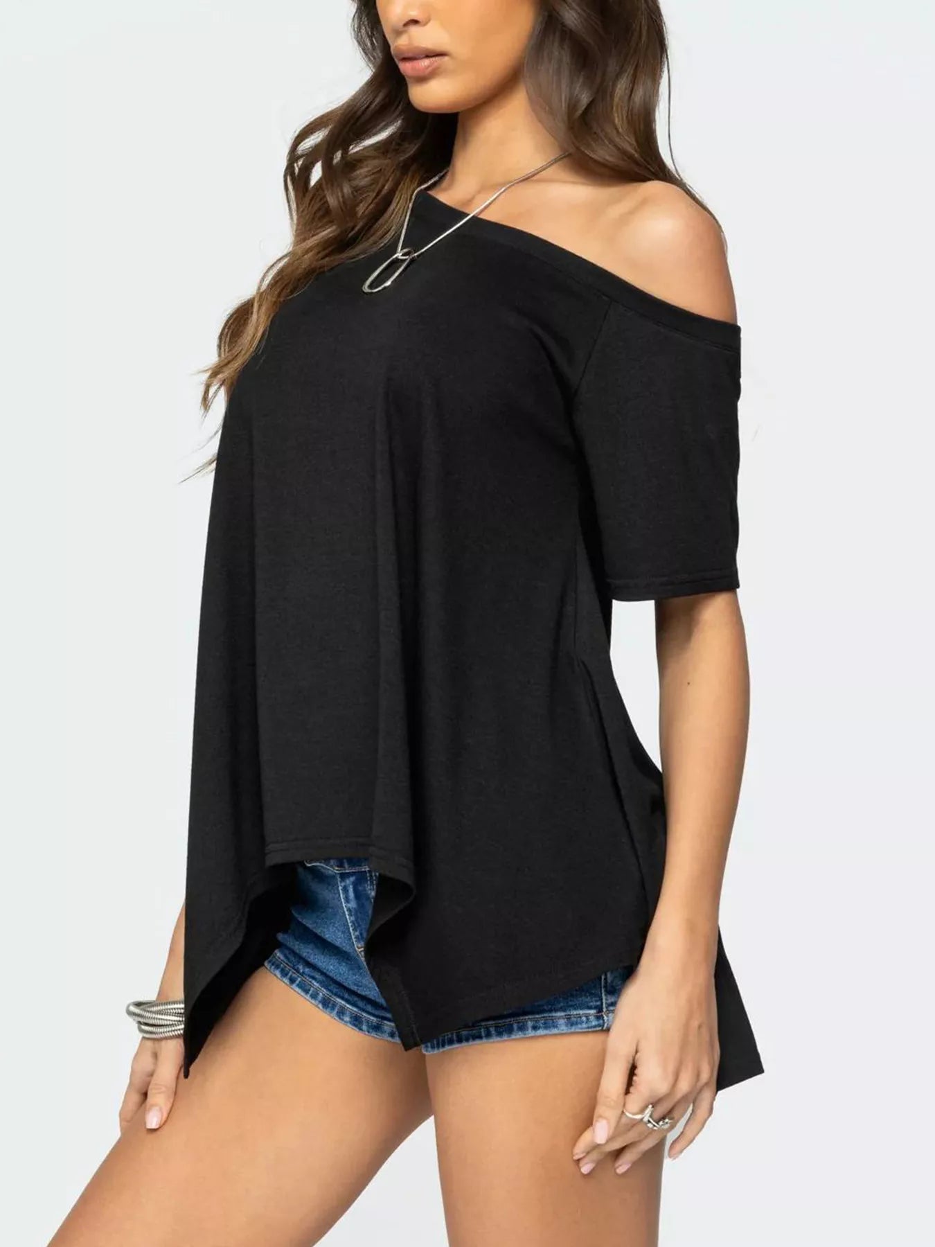 Woman wearing a black off-shoulder top and denim shorts on a white background