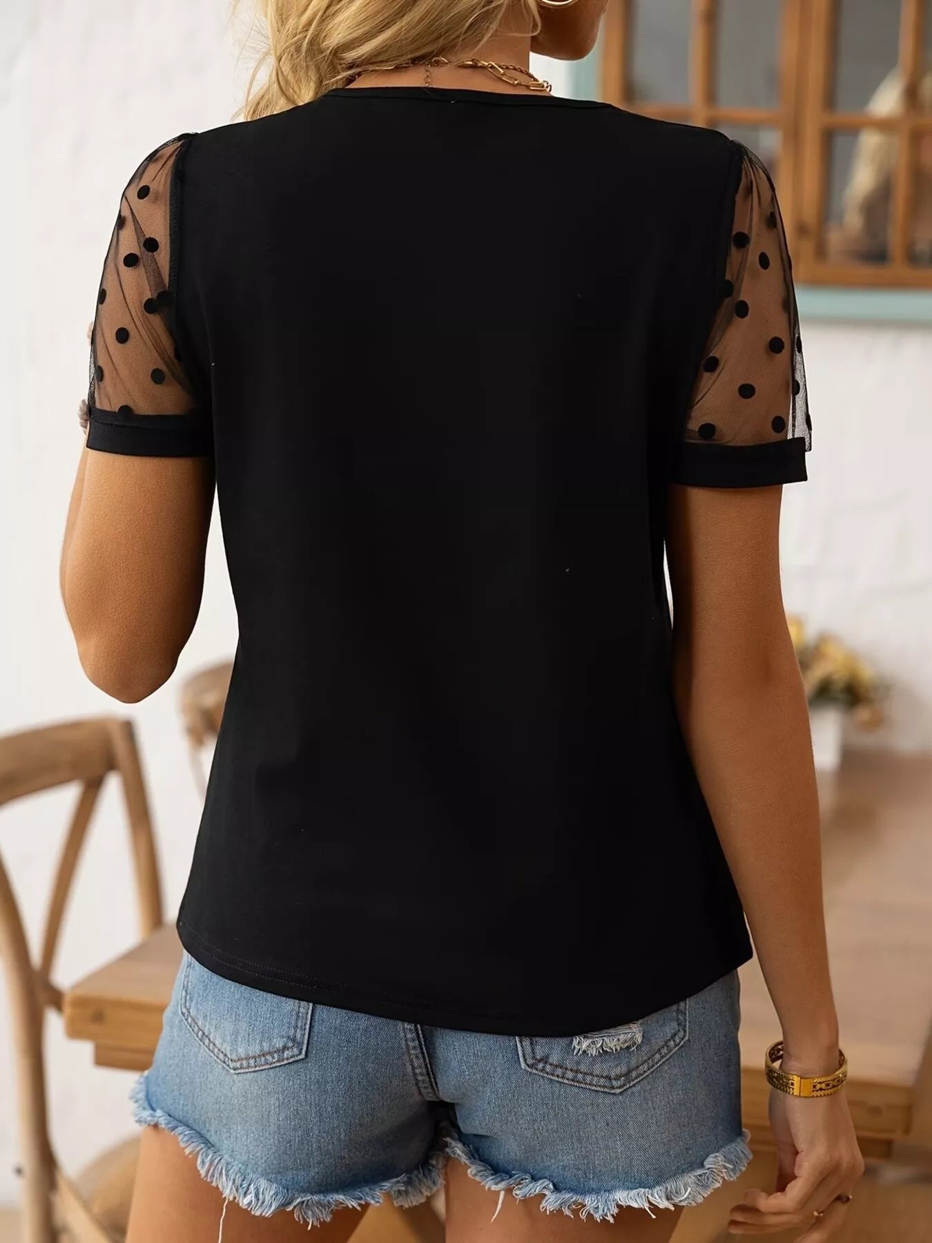 Black top with sheer sleeves and denim shorts worn by a person indoors.