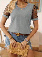 Woman wearing a gray t-shirt with sheer sleeves, denim shorts, and holding a yellow clutch.