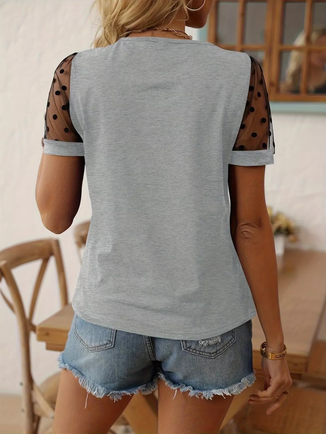 Person wearing a gray sleeveless top with polka dot sleeves and denim shorts in an indoor setting.