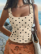 Woman wearing a beige tank top with black polka dots by the ocean.