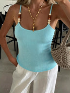 Person wearing a light blue tank top with a necklace and holding a woven bag.