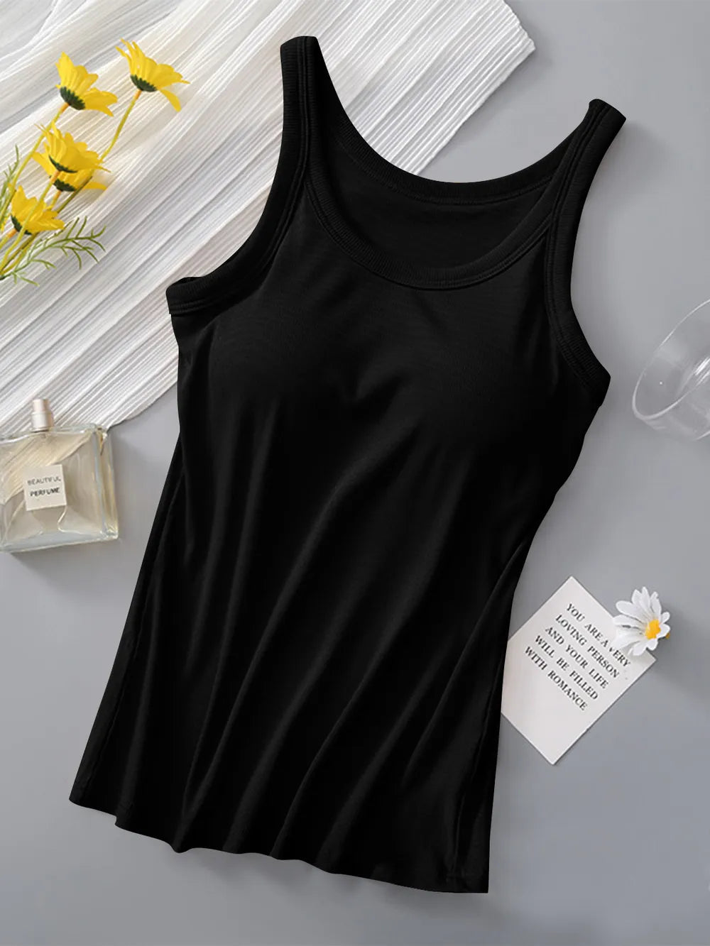 Black tank top on a gray surface with yellow flowers and a glass of water in the background.