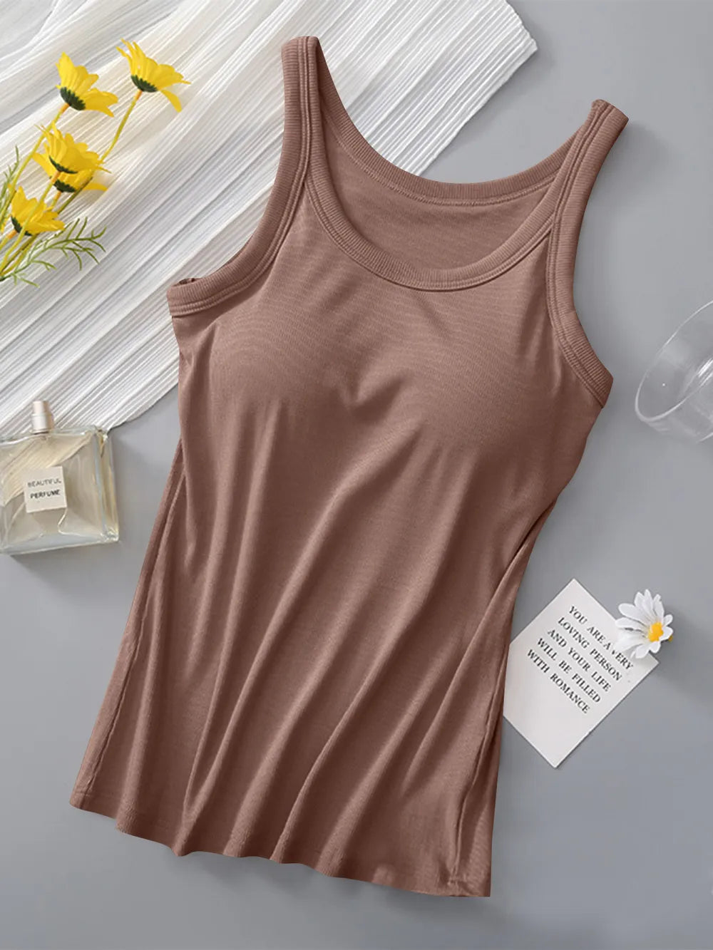 Brown tank top on a gray surface with yellow flowers and a glass of water in the background.