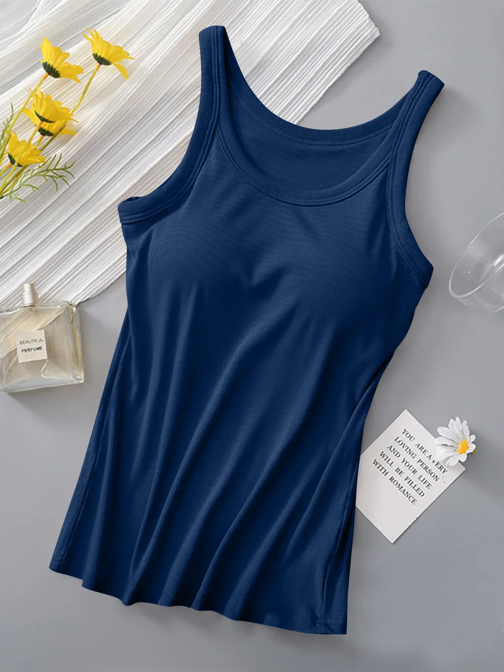Navy blue tank top on a gray surface with yellow flowers and a glass of water in the background.