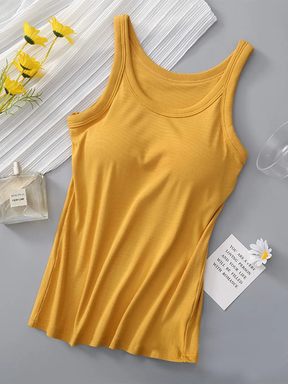 Yellow tank top on a gray surface with flowers and a glass of water in the background