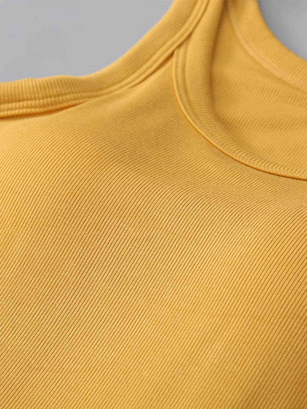 Close-up of a mustard yellow sleeveless top with a gray background