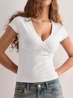 Woman wearing a white V-neck top and blue jeans on a plain background