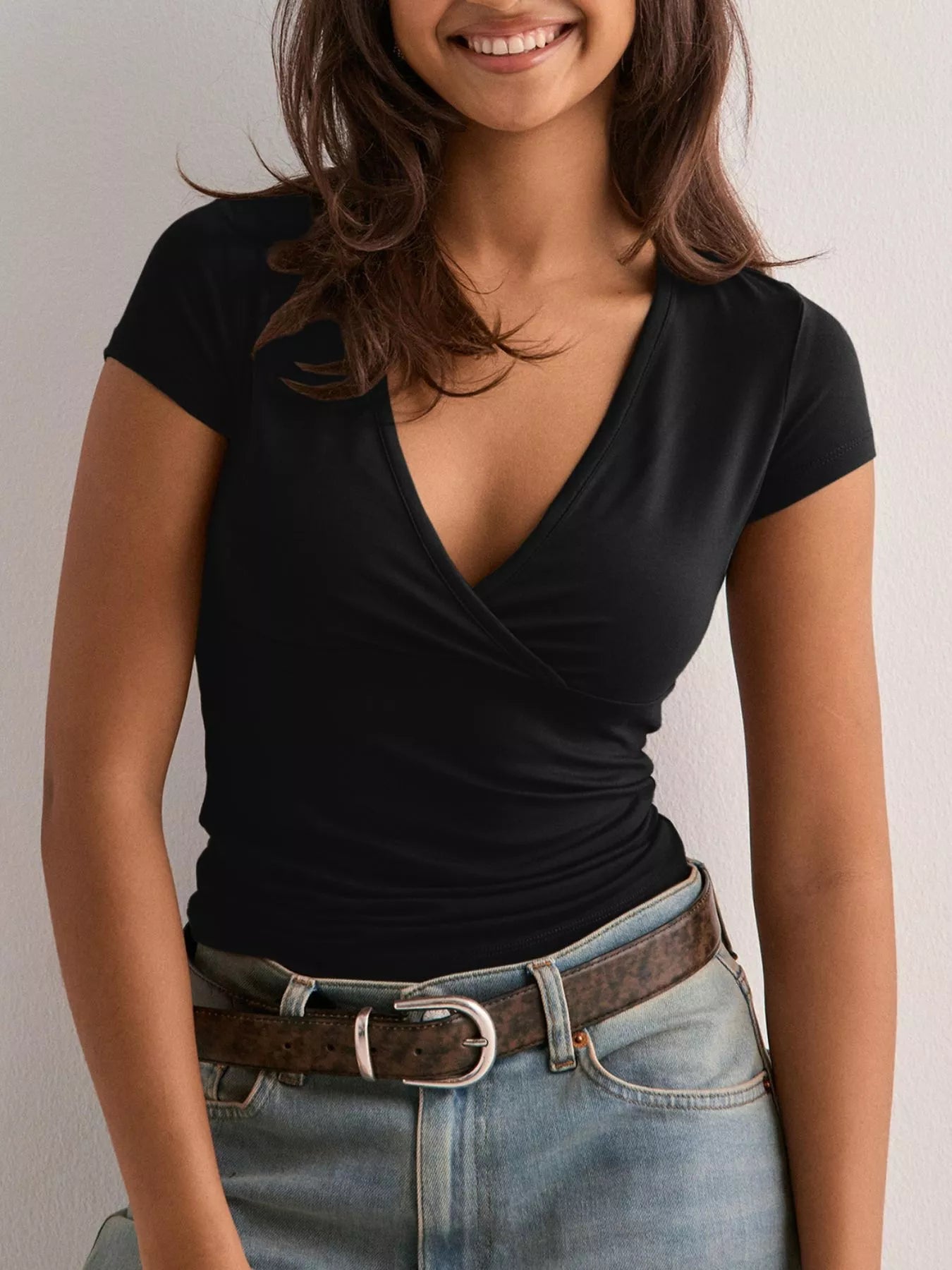 Woman wearing a black top and blue jeans with a belt against a plain background