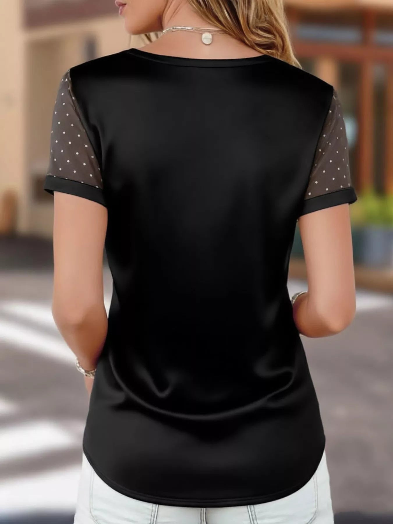 Black short-sleeve top with mesh sleeves worn by a person, blurred background