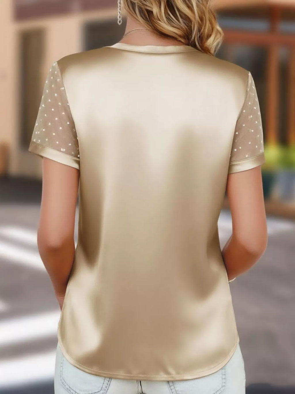 Beige satin top with sheer sleeves worn by a person, blurred background