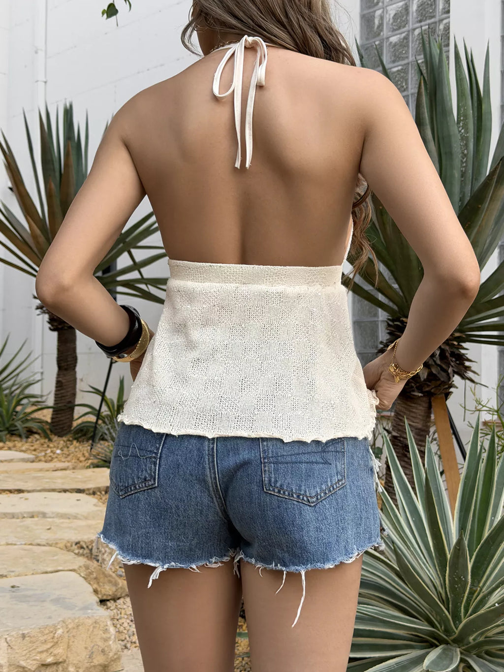 Woman wearing a white top and denim shorts with plants in the background