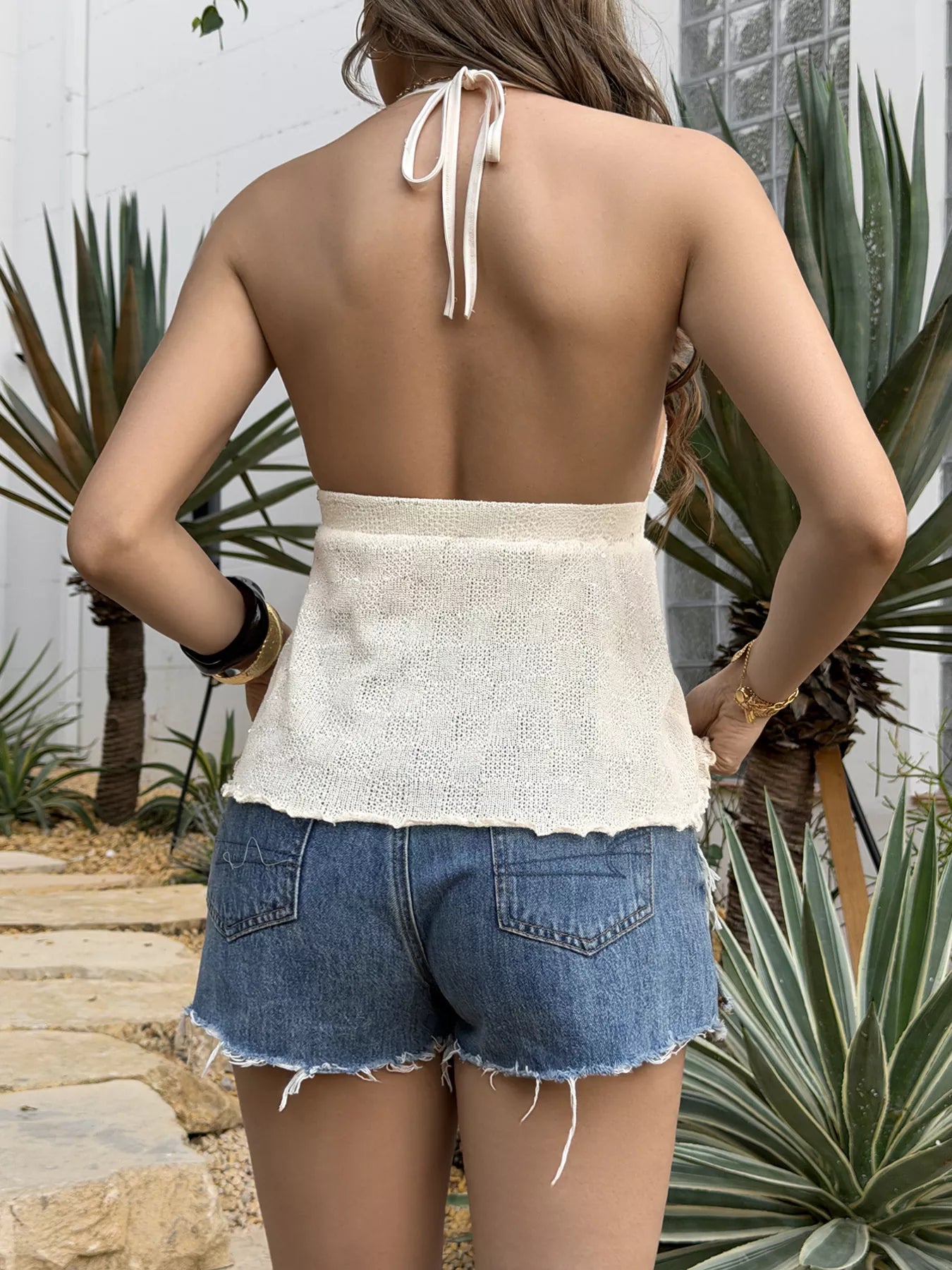 Woman wearing a white top and denim shorts with plants in the background