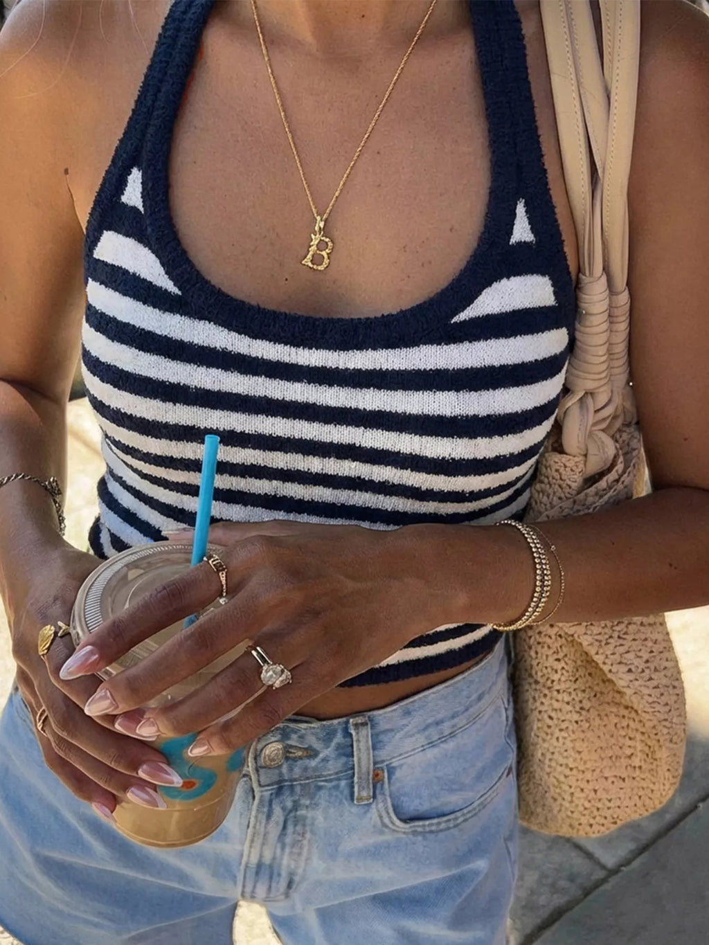 Person wearing a striped tank top and holding a drink with a straw.