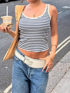 Person wearing a striped tank top and jeans, holding a drink on a street.