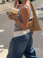 Person wearing a striped tank top and jeans, holding a drink on a street.