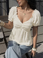 Woman wearing a white blouse with puffed sleeves sitting outdoors.