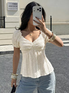 Woman taking a mirror selfie wearing a white textured top and blue jeans.